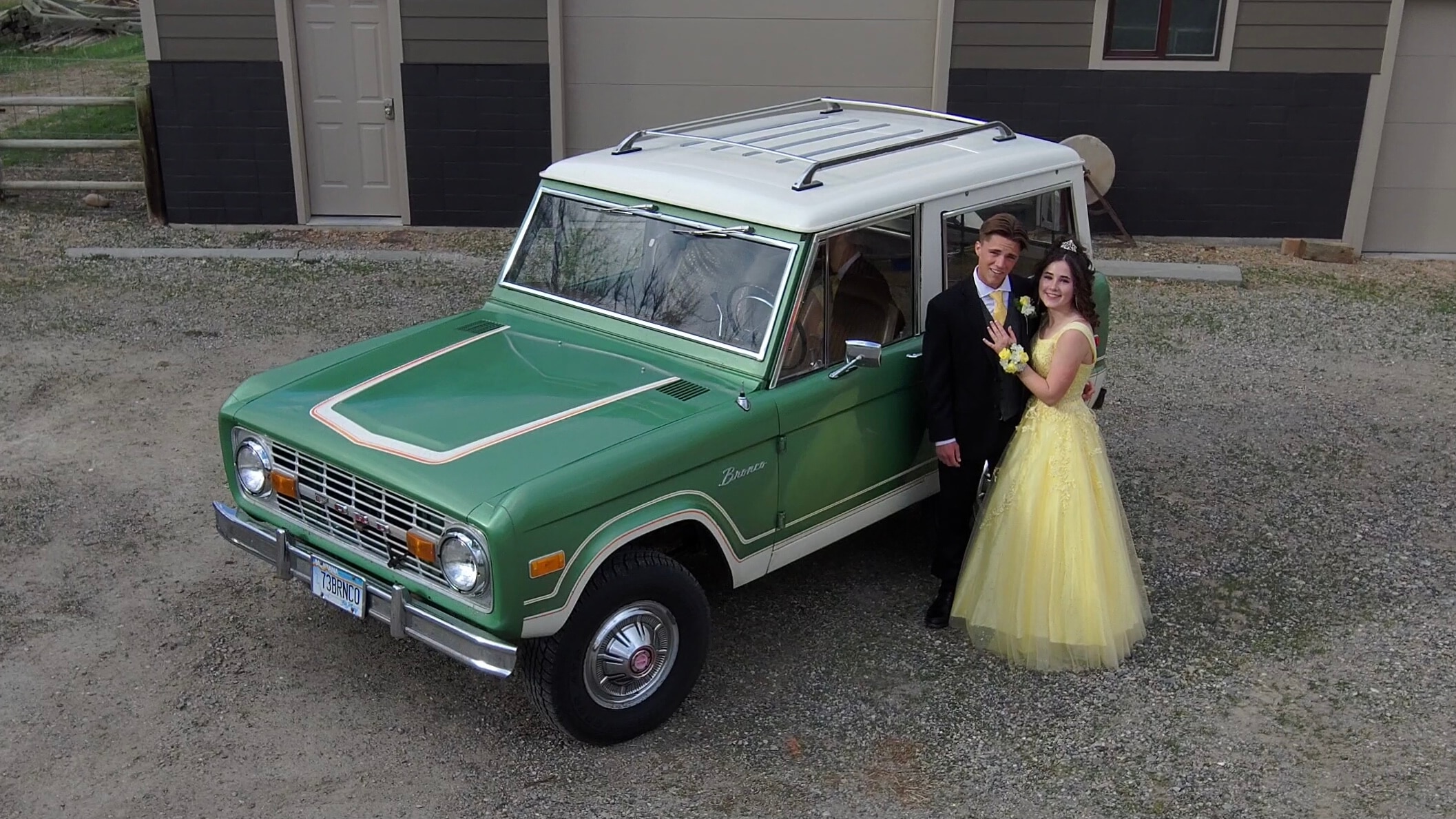 A couple poses in prom attire in front of a green Ford Bronco